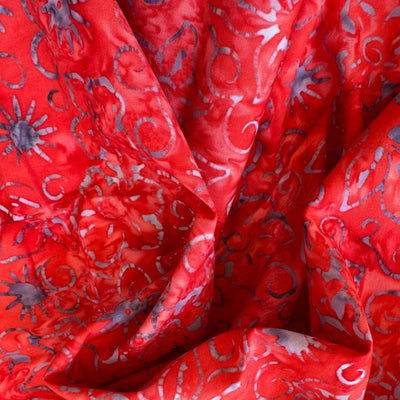 Tela batik soles y arabescos lila sobre rojo vivo