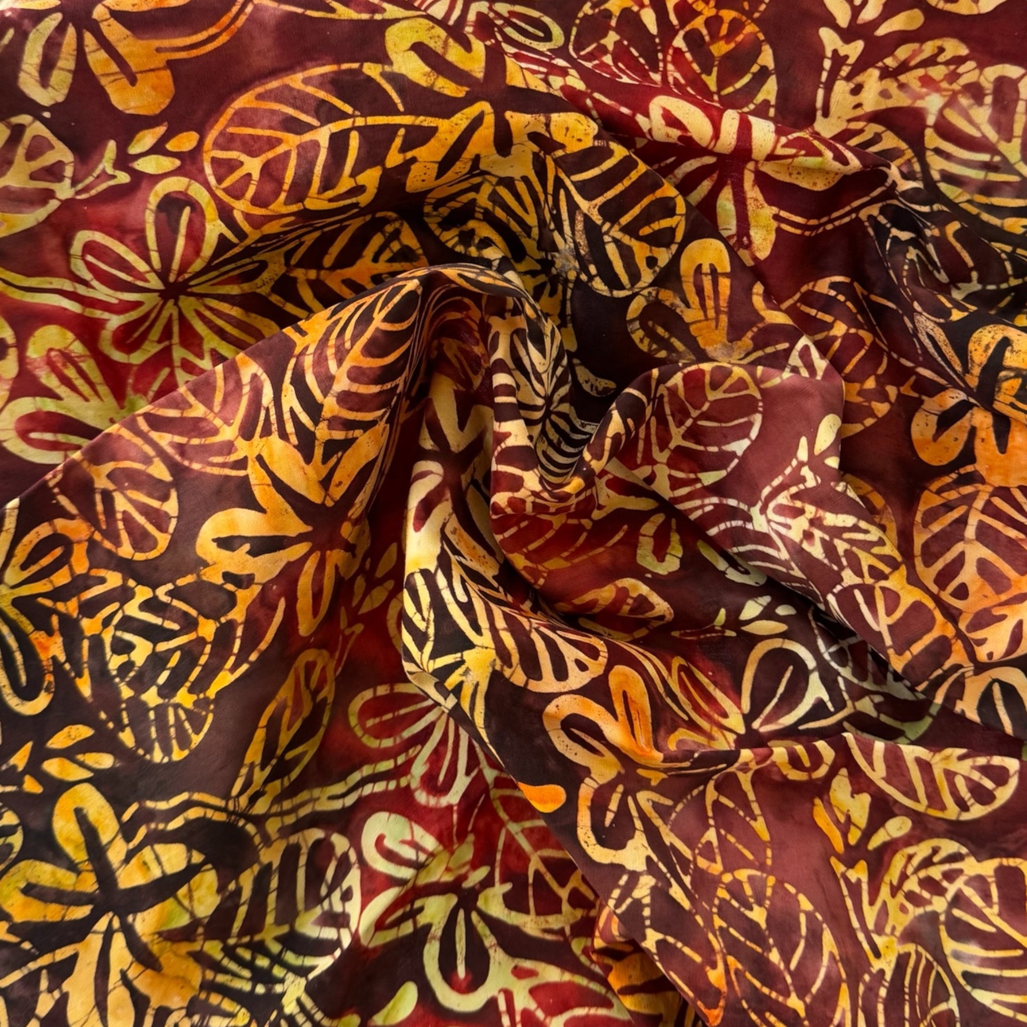 Tela batik hojas tropicales granate y dorado